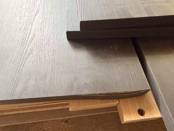 Comparison of properly bonded edge banding and locally lifted edge banding on dark wood-grain cabinet panels.