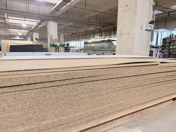 Stacked particleboard panels with exposed edges inside a custom cabinet factory