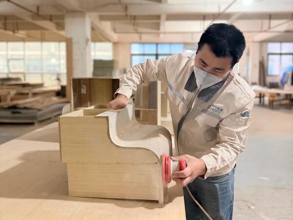 Worker sanding a curved wood veneer cabinet component before veneer application
