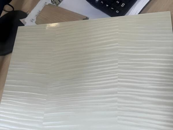 Close-up of a light-colored melamine surface sample showing its wood-grain texture