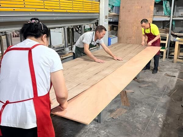 Workers laying natural wood veneer on a panel before hot pressing in the factory
